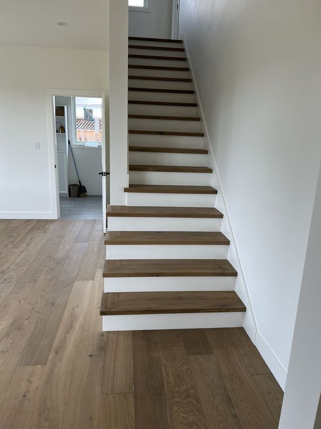 A white staircase with wooden steps leading up to the second floor of a house.