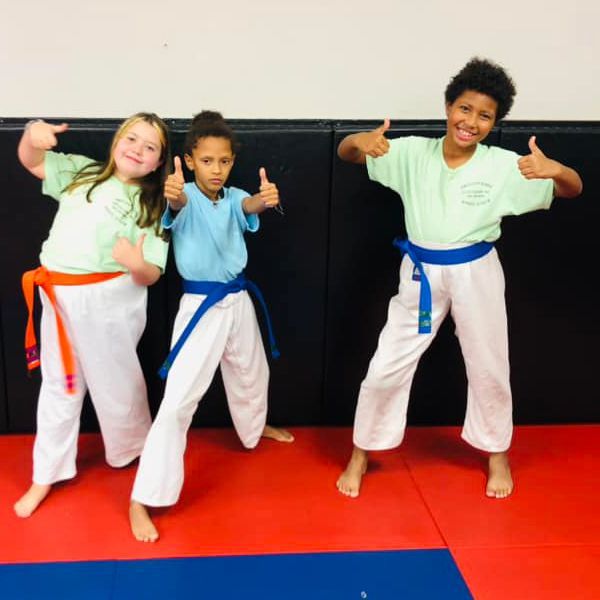 three young girls in karate uniforms are giving a thumbs up .
