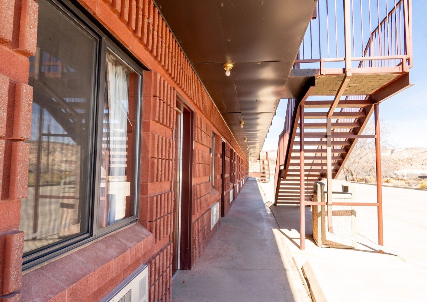 Exterior walkway of a brick building with windows and an outdoor staircase on the right