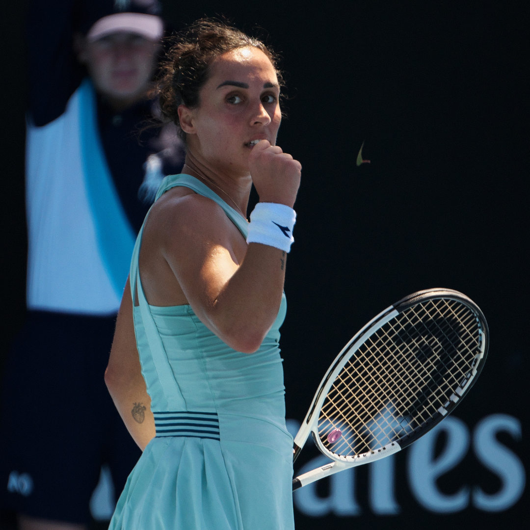 Tennista in abito blu-verde che stringe il pugno con la racchetta in campo, si morde il labbro e festeggia.