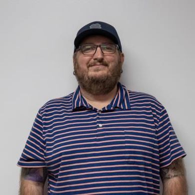 A man with a beard and glasses is wearing a striped shirt and a hat.