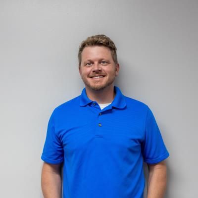A man in a blue shirt is standing in front of a white wall.
