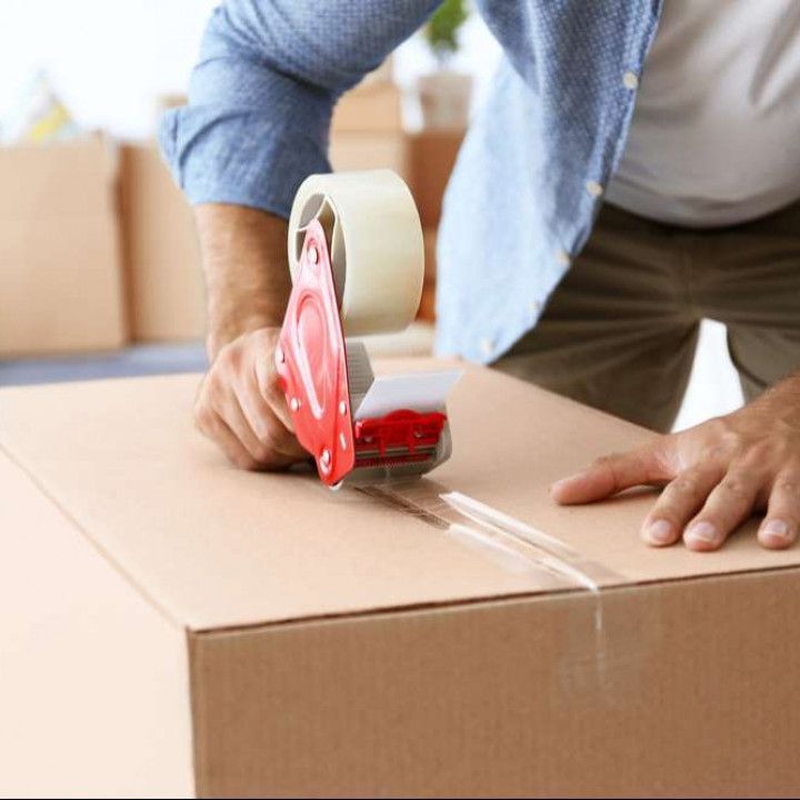 a man is using a tape dispenser to seal a cardboard box .