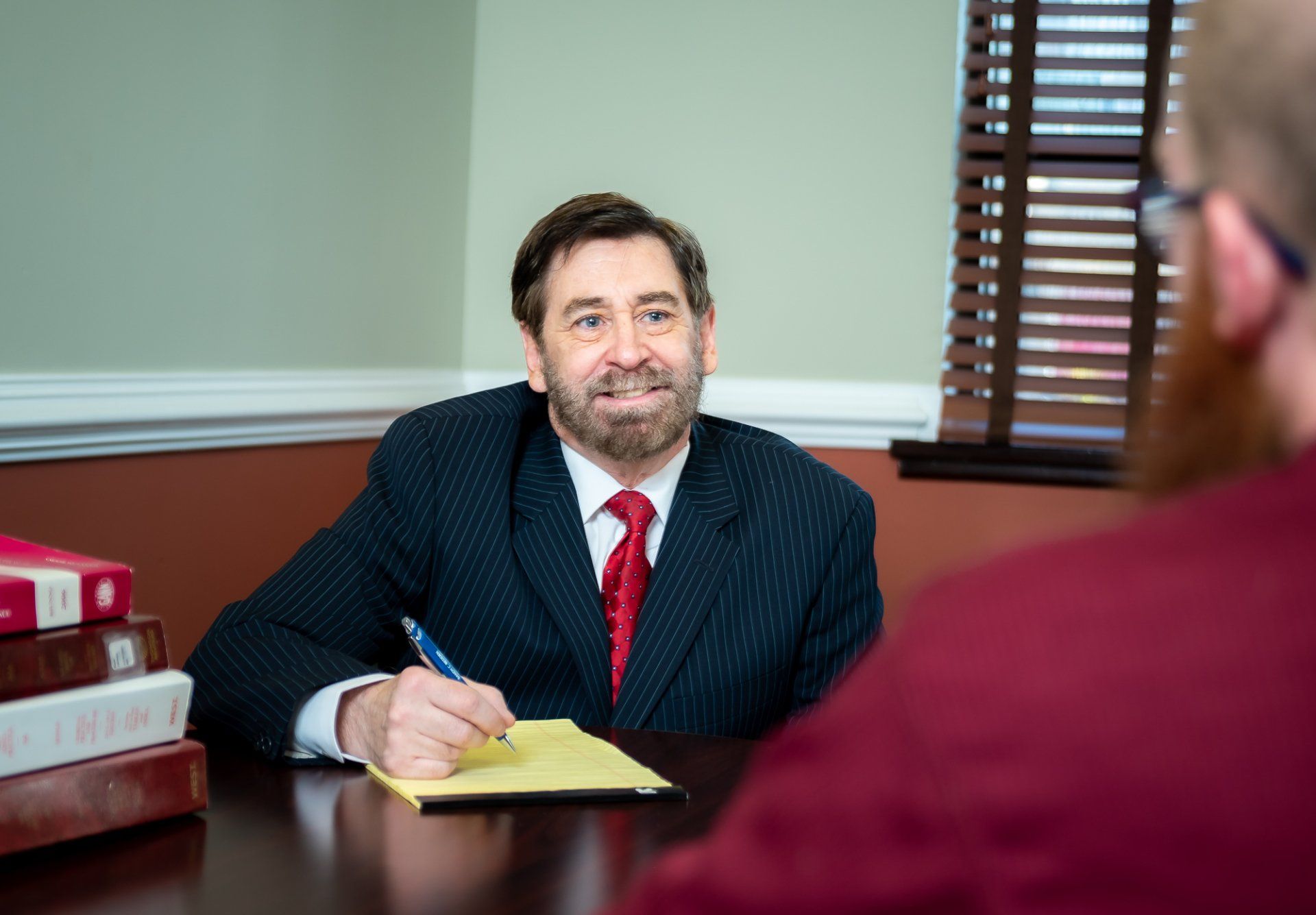 A man in a suit and tie is sitting at a table talking to another man.