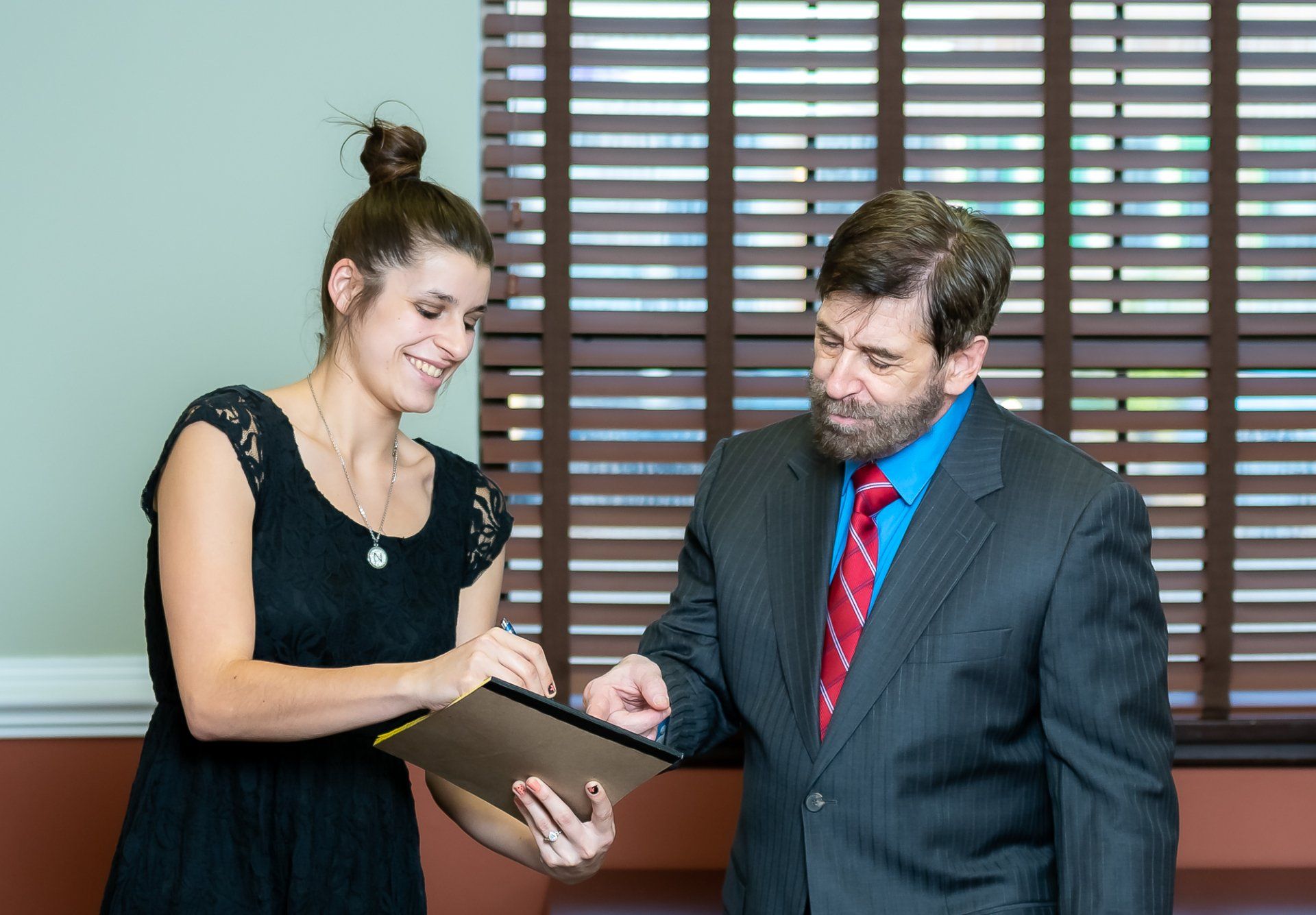 A man in a suit and tie is standing next to a woman holding a clipboard.