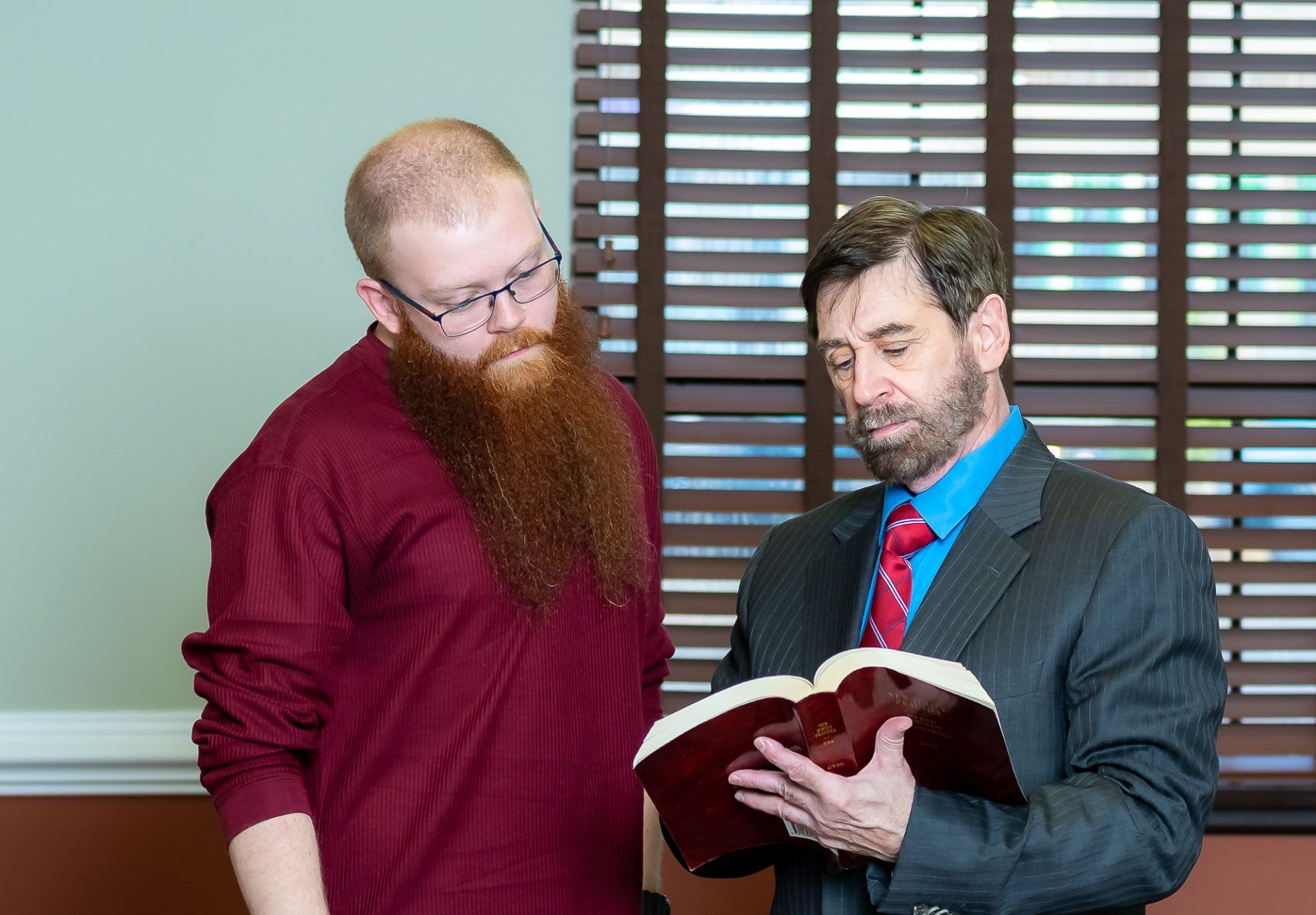 Two men are standing next to each other looking at a bible.