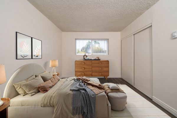 Bright bedroom with a bed, dresser, window, and closet doors in neutral tones