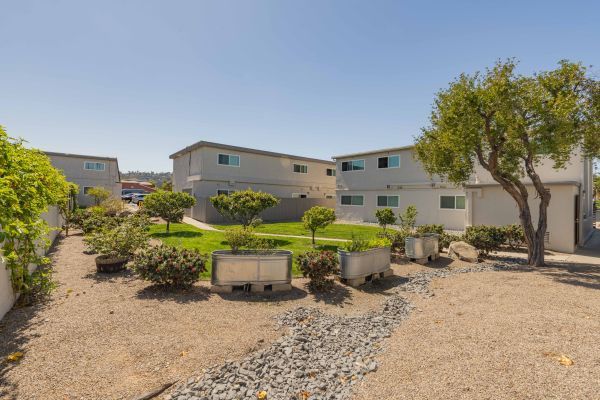 Desert courtyard with gravel, shrubs, trees, and beige apartment buildings under a clear blue sky