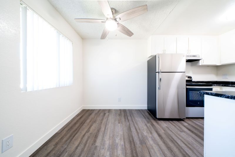 Empty bright kitchen with white cabinets, stainless steel fridge, and wood-look flooring