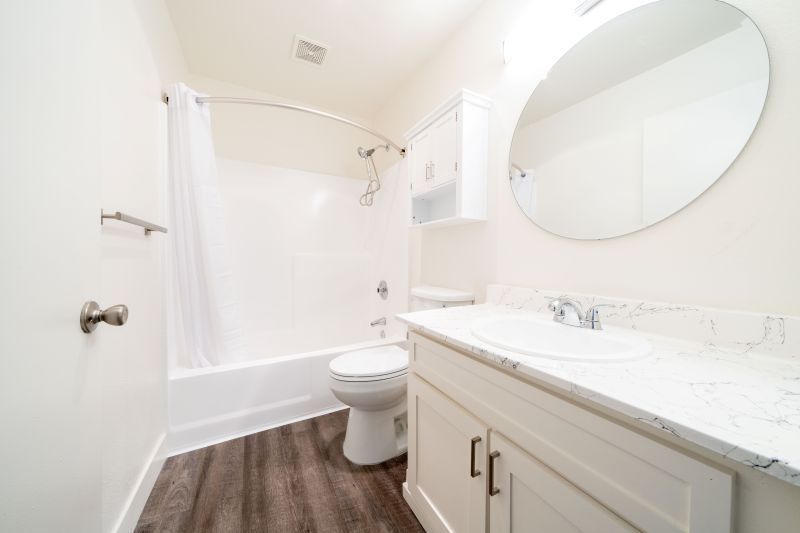 Bright white bathroom with bathtub, toilet, vanity, and round mirror