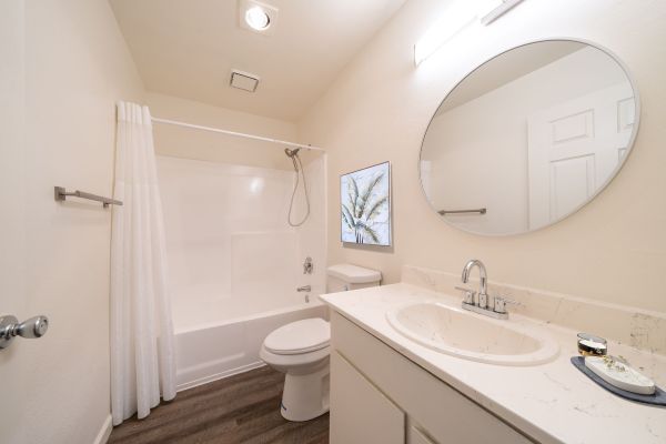 Bright, modern bathroom with white tub, vanity, round mirror, and wood-look floor.