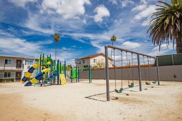 Empty playground with slides, swings, and a climbing frame on sandy ground under a blue sky