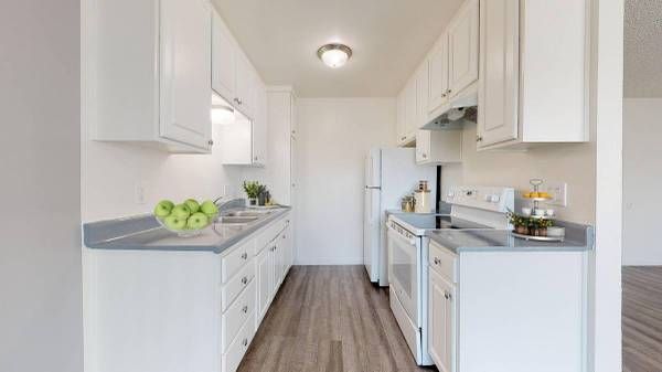 Bright white galley kitchen with gray countertops, wood-look floor, and a refrigerator at the back.