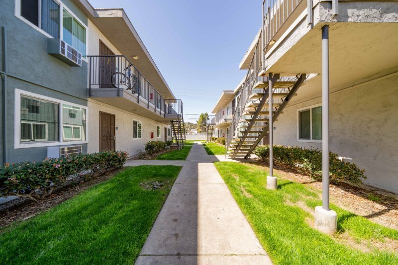 Apartment courtyard with sidewalks, green lawns, and exterior staircases between beige buildings