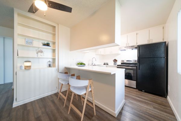 Bright modern kitchen with white cabinets, breakfast bar, black fridge, and wood flooring