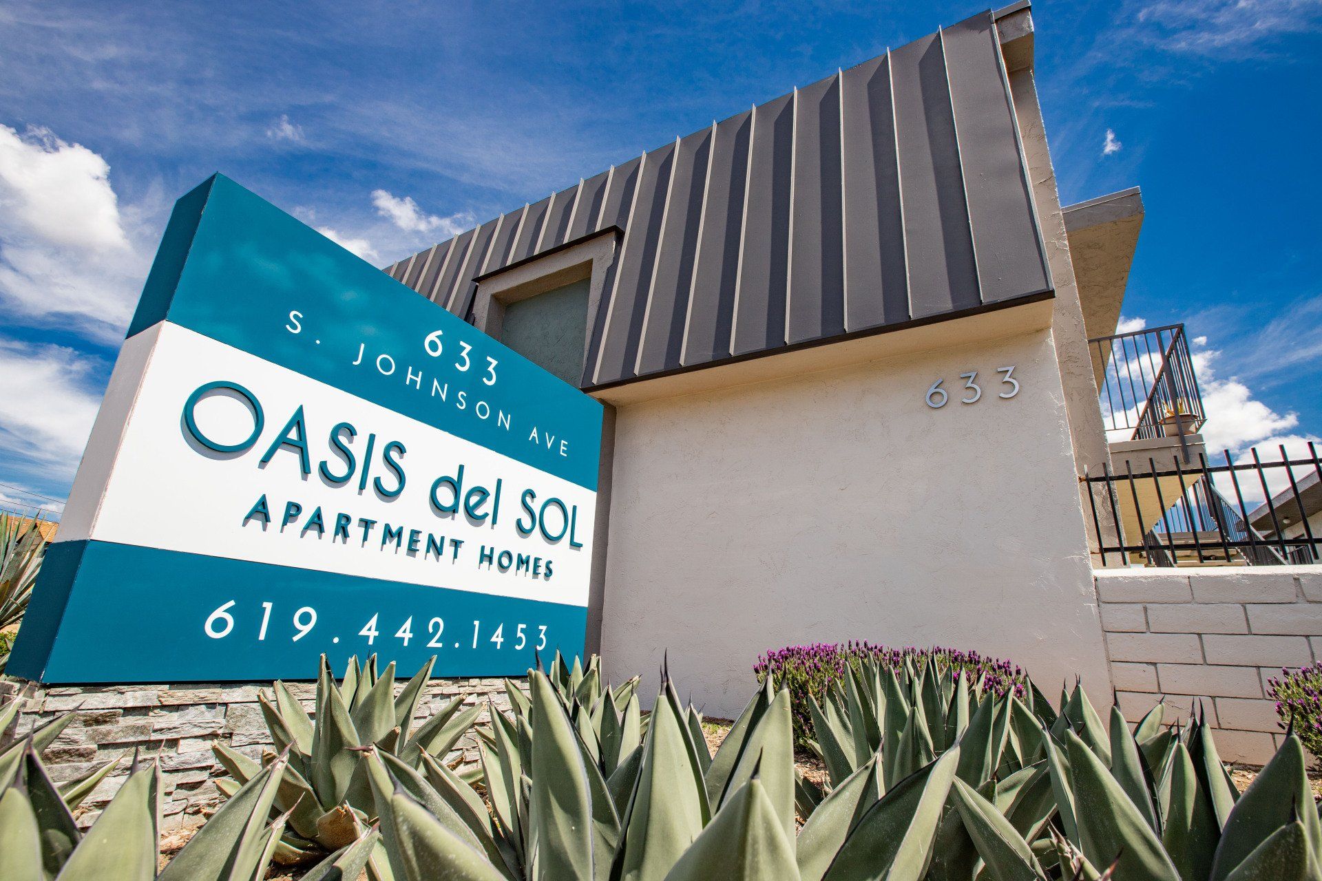 Oasis del Sol Apartment Homes sign outside modern building with agave plants and blue sky