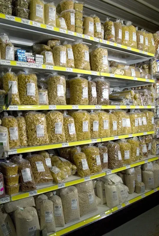 A grocery store shelf filled with various types of bulk pasta and dry goods in clear plastic bags.