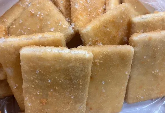 A pile of rectangular, golden-brown crackers covered in small, coarse crystals of sugar.