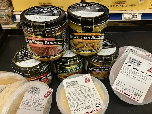 A shelf display of jars of Better Than Bouillon and plastic containers of deli salad from Perry's Country Store.