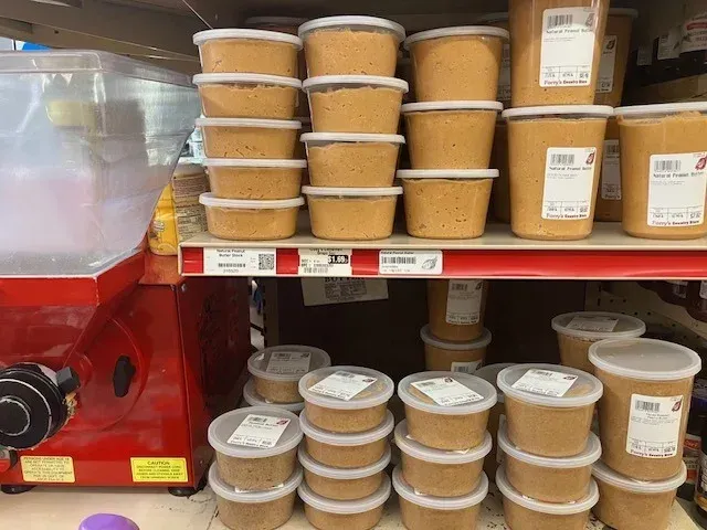 Shelves stocked with many small, plastic containers of tan-colored food products and a red food grinder on the left.