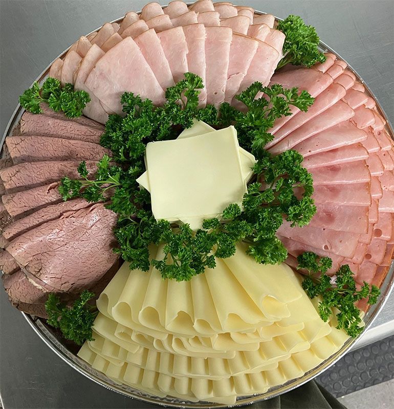 A round party platter arranged with sliced ham, roast beef, and folded cheese, garnished with fresh parsley.