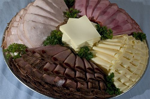 A circular catering tray featuring sections of sliced meats, folded deli cheese, and square cheese slices with parsley.