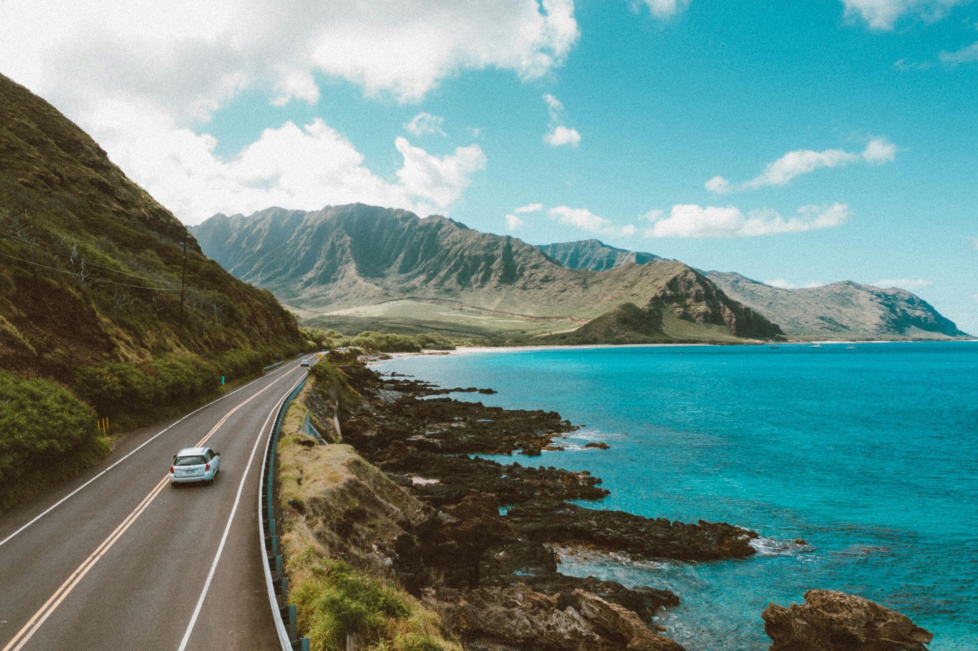 A luxury car is driving down a road next to the ocean in Europe.
