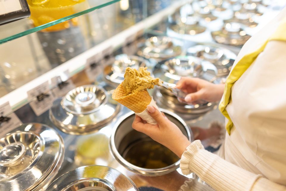 Una persona versa il gelato al pistacchio in un cono da un contenitore di acciaio inossidabile in una gelateria.