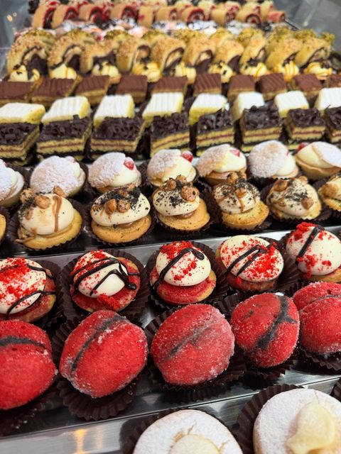 File di mini pasticcini assortiti in una vetrina. I dessert includono rosso, bianco e marrone, con vari condimenti.