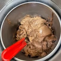 Gelato al cioccolato in una gelatiera di metallo con una spatola rossa.