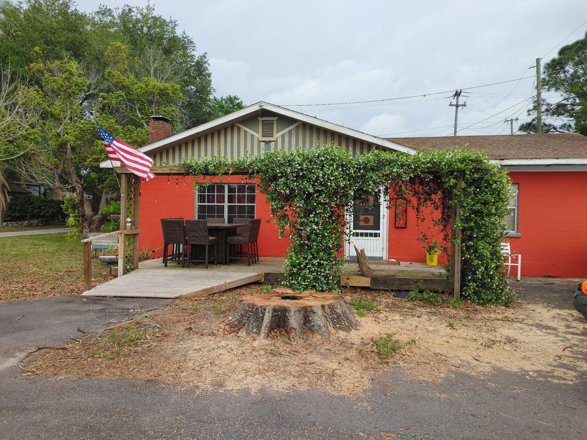 Red house with wooden porch, archway covered in plants. American flag.