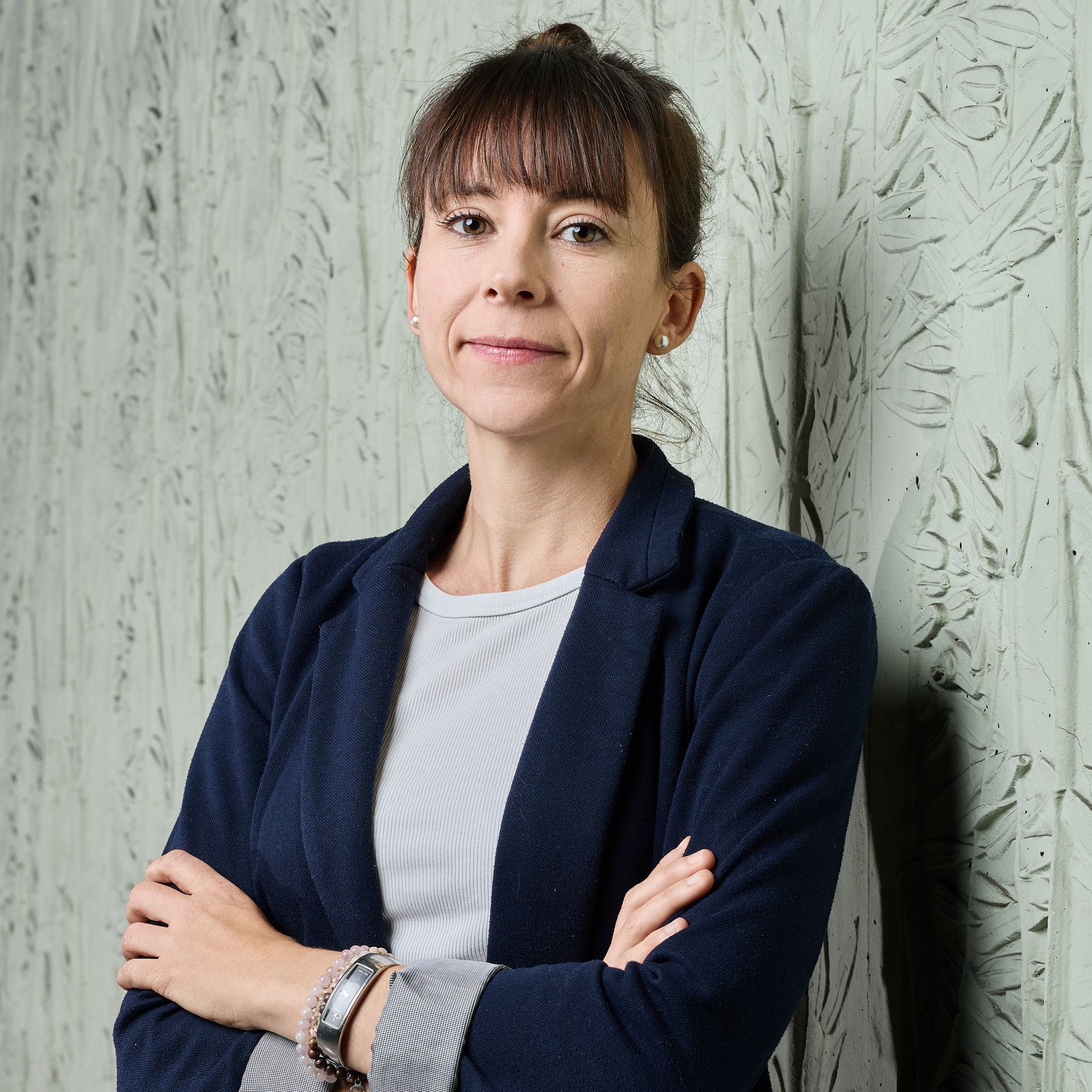 Portrait d'une femme en blazer bleu marine, les bras croisés, devant un mur texturé.