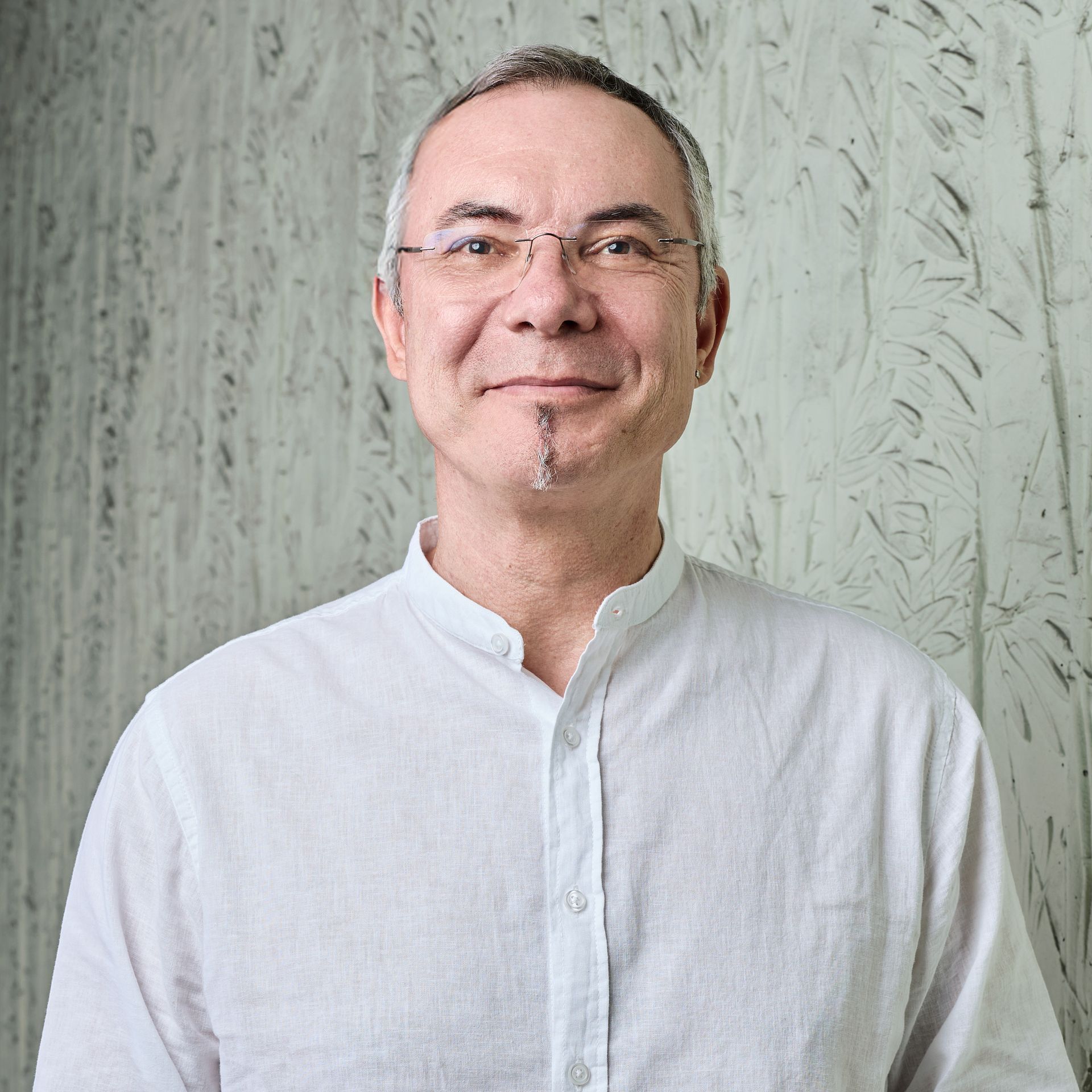 Portrait d'une personne souriante en chemise blanche devant un mur gris texturé