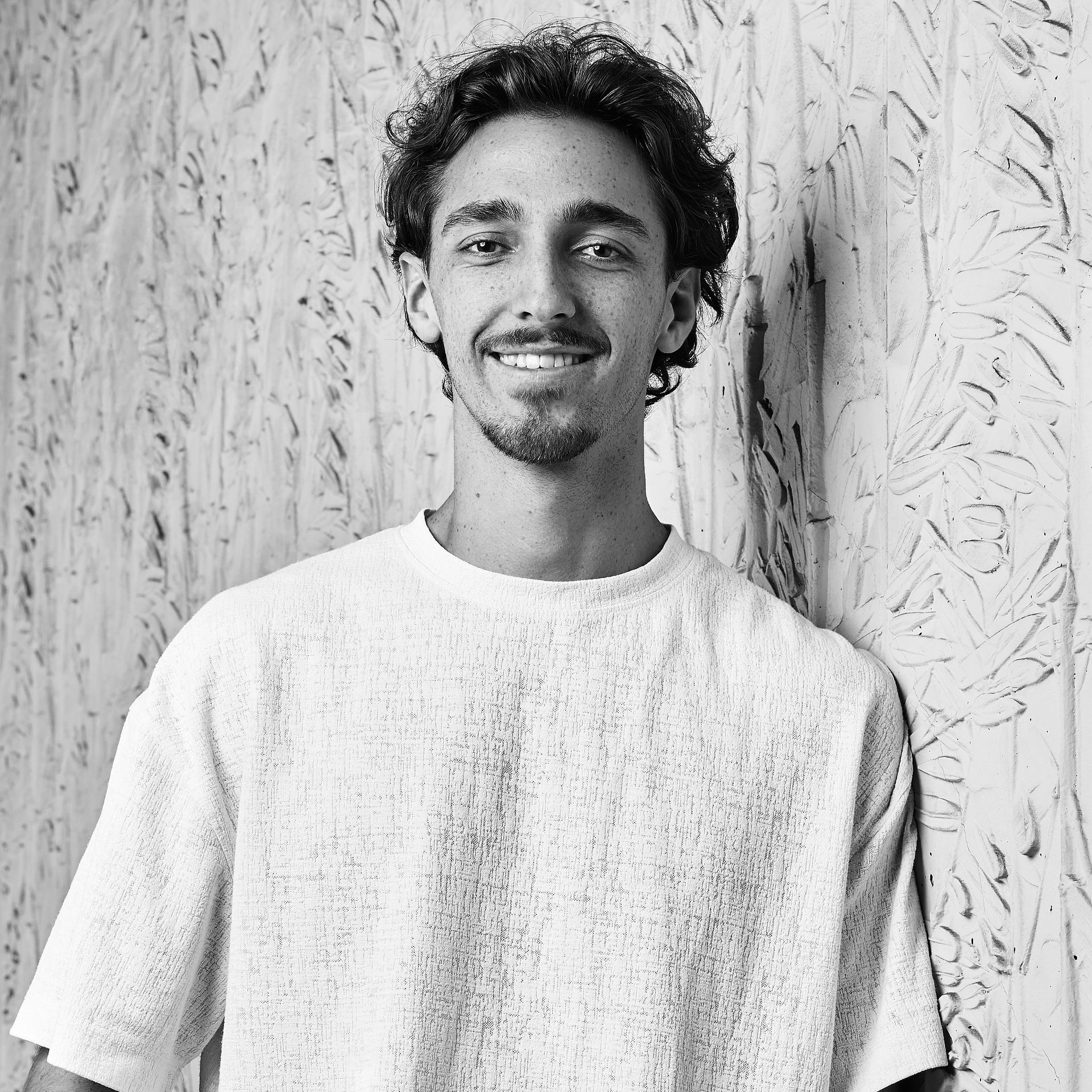 Personne souriante en chemise blanche devant un mur à la texture claire