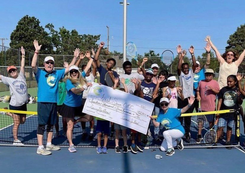Group of people cheering on a tennis court, holding a banner and raising their arms in celebration.