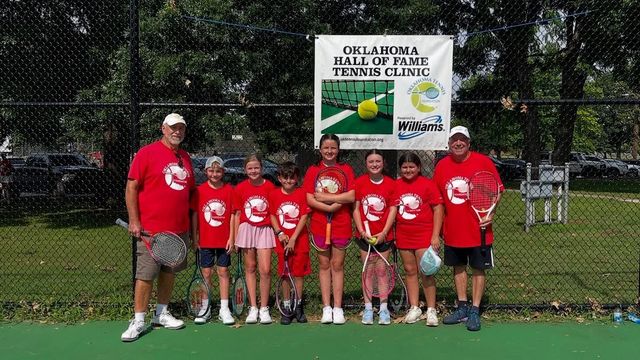 Youth tennis team in red shirts posing with coach on a court in front of a banner