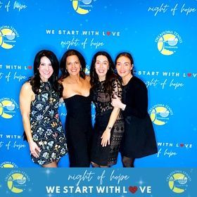 Four women pose in front of a blue 