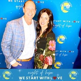 Two people posing at a “Night of Hope” event in front of a blue “We Start With Love” backdrop.