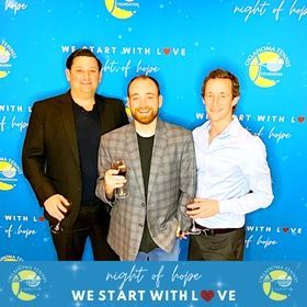 Three men posing with drinks at a blue “Night of Hope” event backdrop