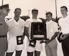 Five people in white sportswear pose with trophies and a framed award plaque.