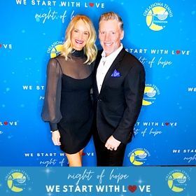Two people posing on a blue step-and-repeat backdrop with “Night of Hope” and “We Start With Love” logos.