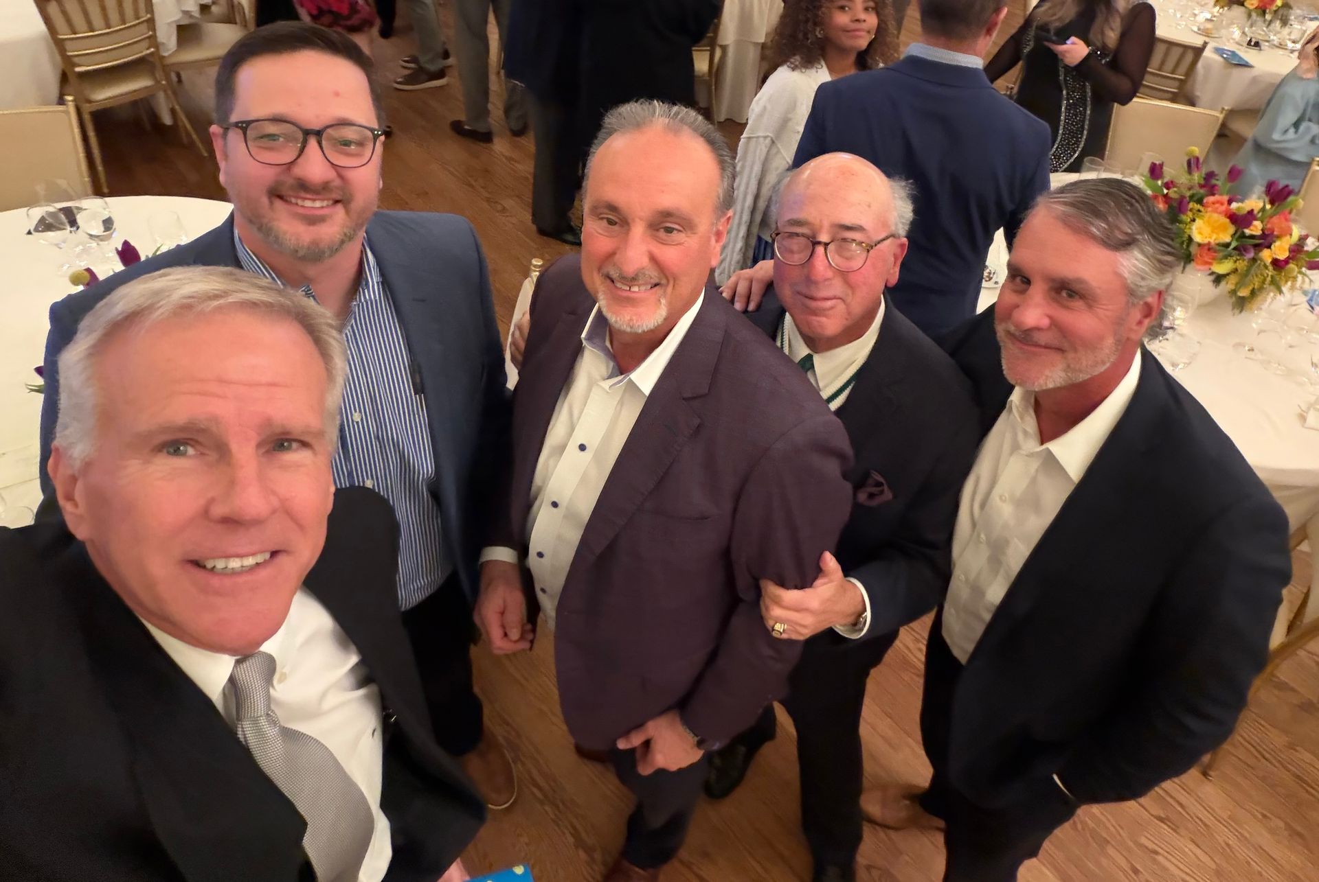 Five men in suits smiling and posing together at a formal indoor event