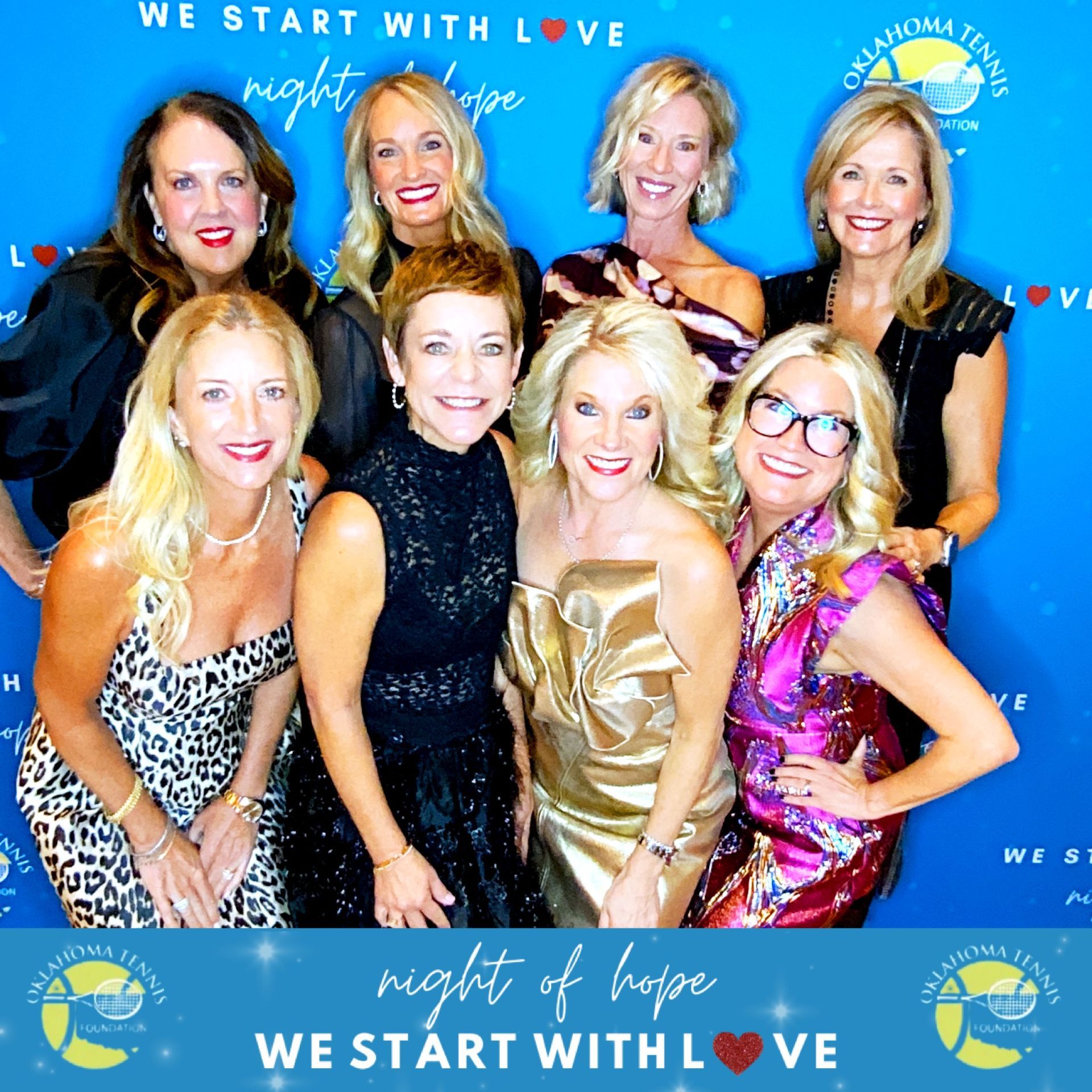 Group of smiling women posing at a “Night of Hope” event with a blue backdrop and red carpet.