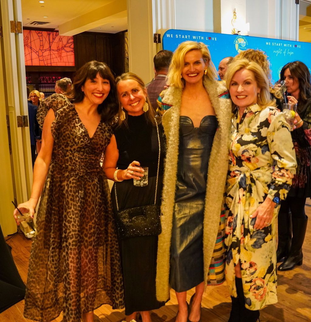 Four women posing and smiling at an indoor event, dressed in formal evening attire.