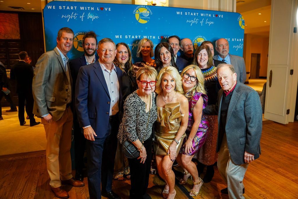 Group of people posing indoors at an event in front of a blue backdrop and warm lighting