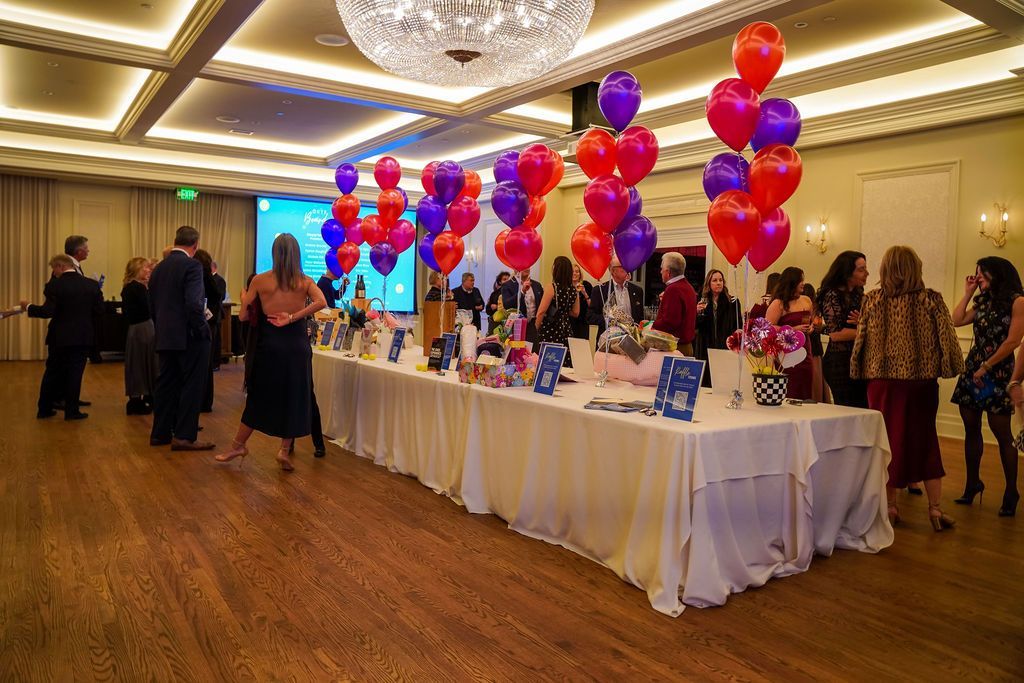 Balloon-decorated event table in a banquet hall with guests mingling nearby