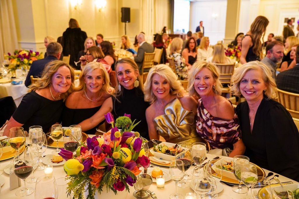 Group of women smiling at a banquet table with a colorful floral centerpiece in a bright event hall