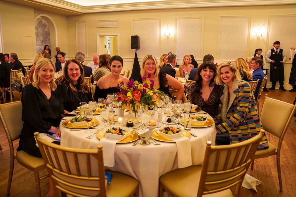 Group seated at a banquet table in a warmly lit event hall, with flowers and plates set for dinner.