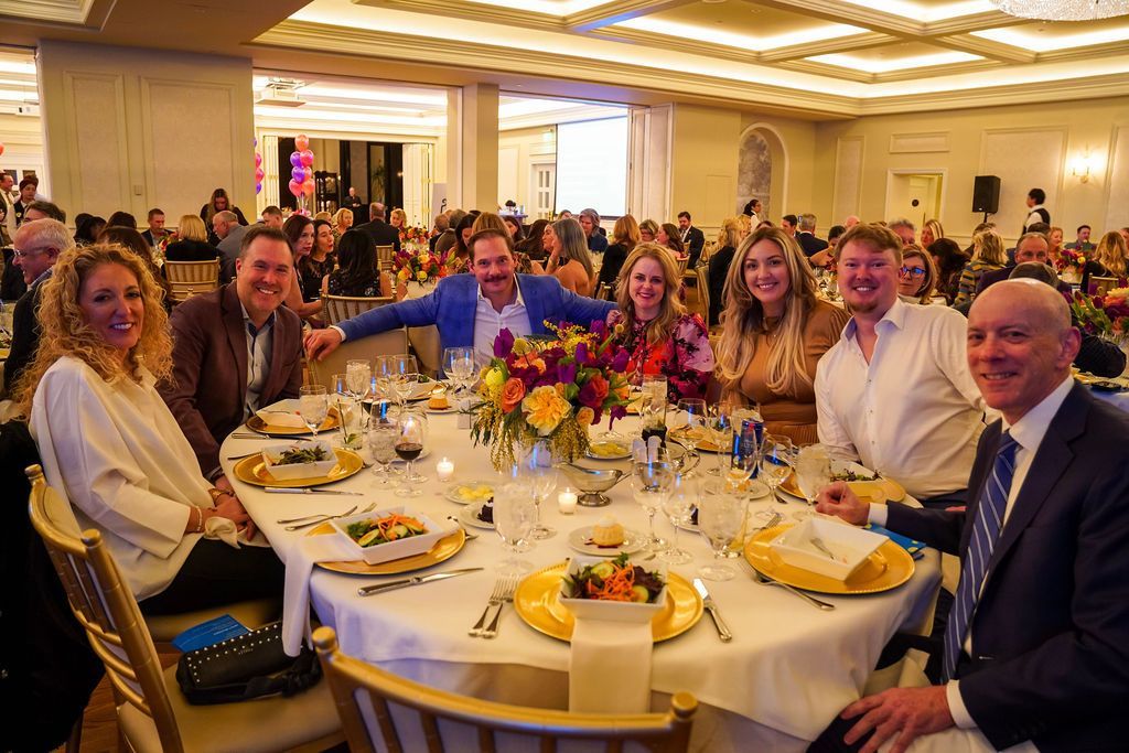 Formal banquet table with eight people smiling under warm ballroom chandeliers