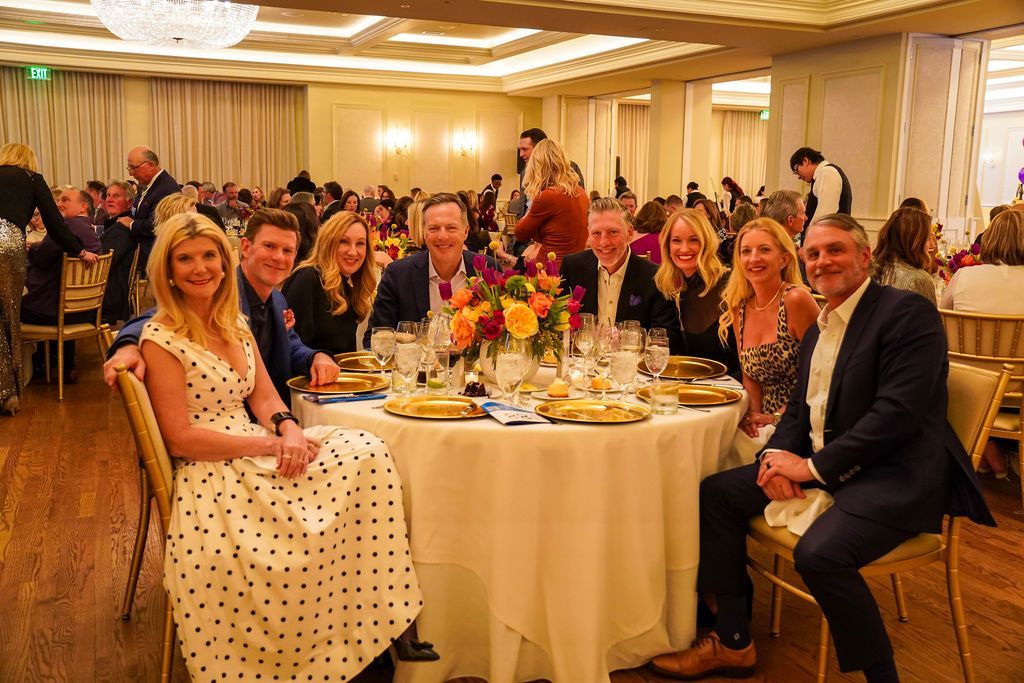 Guests seated at round banquet tables in a warmly lit reception hall, with floral centerpieces and smiling faces